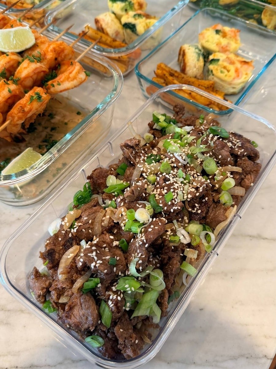A glass meal prep container filled with tender Chinese beef and onion stir fry, garnished with toasted sesame seeds and fresh sliced green onions.