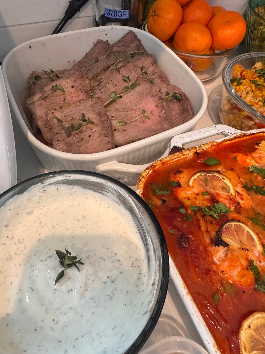 A roast beef platter with horseradish herbs, alongside baked harissa cod with lemon slices, plus a creamy sauce and buttery corn rice side dishes.