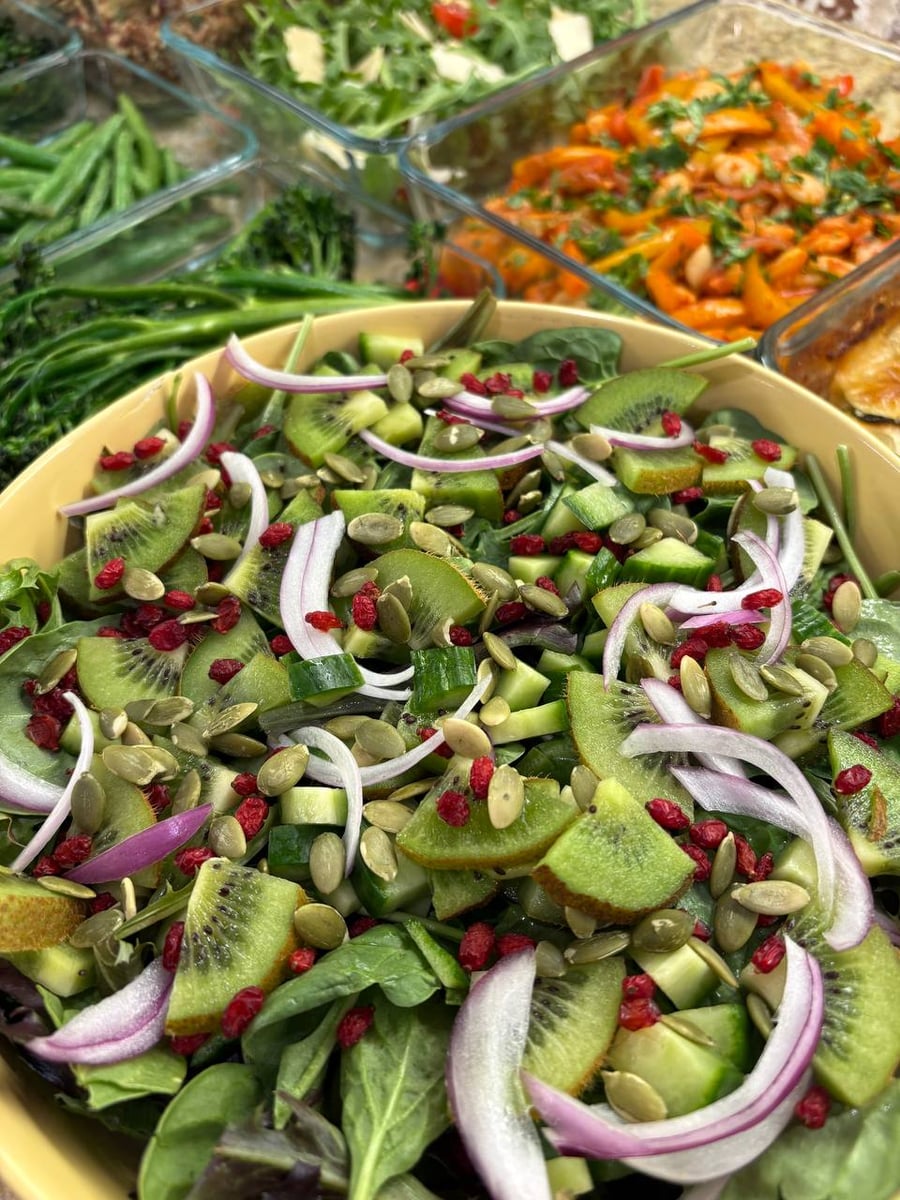 A large yellow bowl features a fresh salad made with sliced kiwi, crisp cucumbers, spinach, red onion, pumpkin seeds, and bright red barberries.