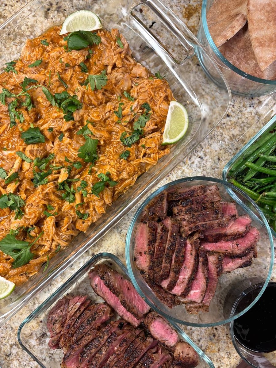 A glass dish of saucy shredded chicken with lime, a bowl of sliced herb-crusted steak, and a side of green beans with pita bread.