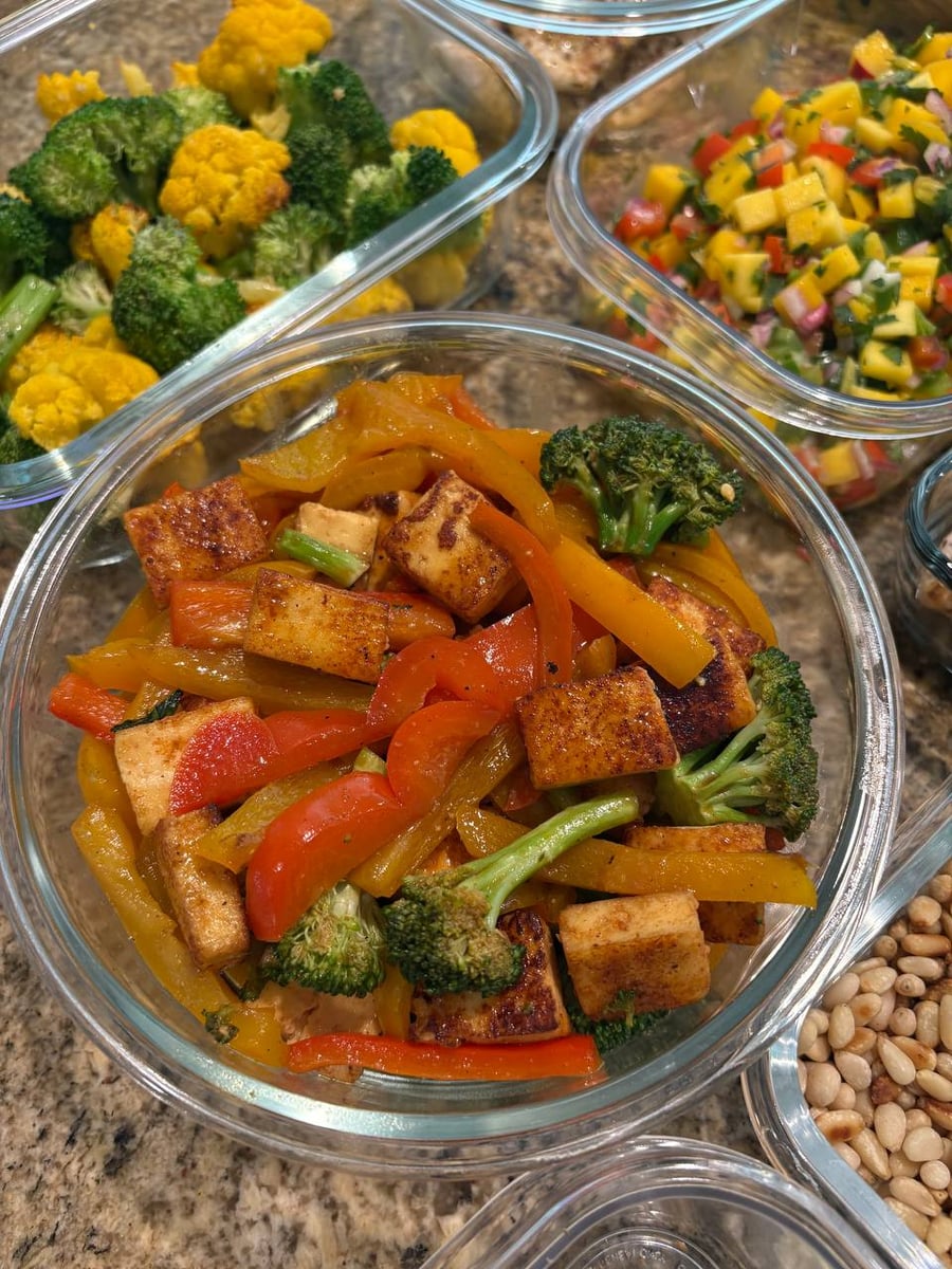 A glass bowl containing a vibrant stir-fry of seared paneer cubes, bright yellow and red bell pepper strips, and tender green broccoli florets.