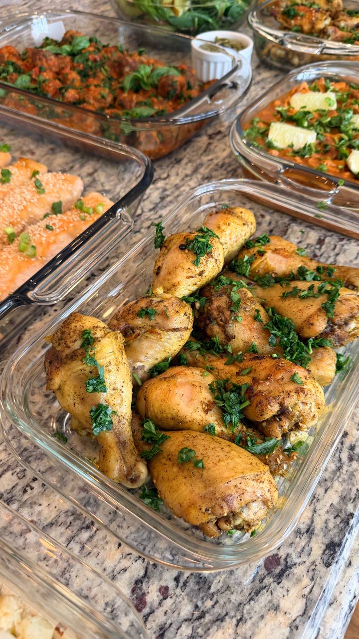 A glass baking dish overflowing with golden roasted chicken drumsticks, seasoned with Mediterranean spices and generously garnished with fresh chopped green parsley.