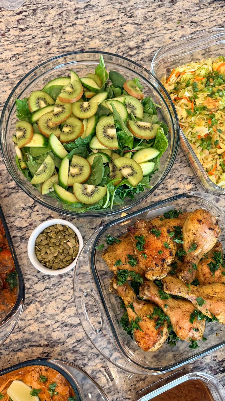 Glass containers featuring Lebanese-style baked chicken drumsticks and thighs garnished with fresh herbs alongside a vibrant fruit and vegetable salad.
