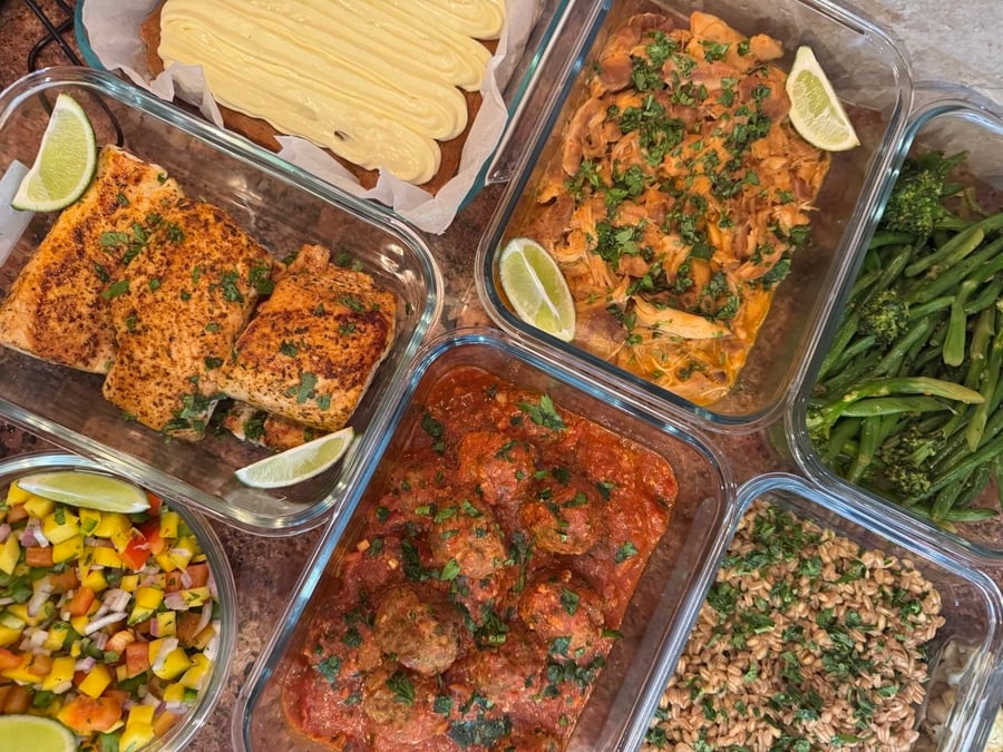Glass containers featuring blackened mahi mahi, shredded chicken, tuscan meatballs, mango salsa, chili crisp green beans, herbed farro, and a carrot cake loaf.