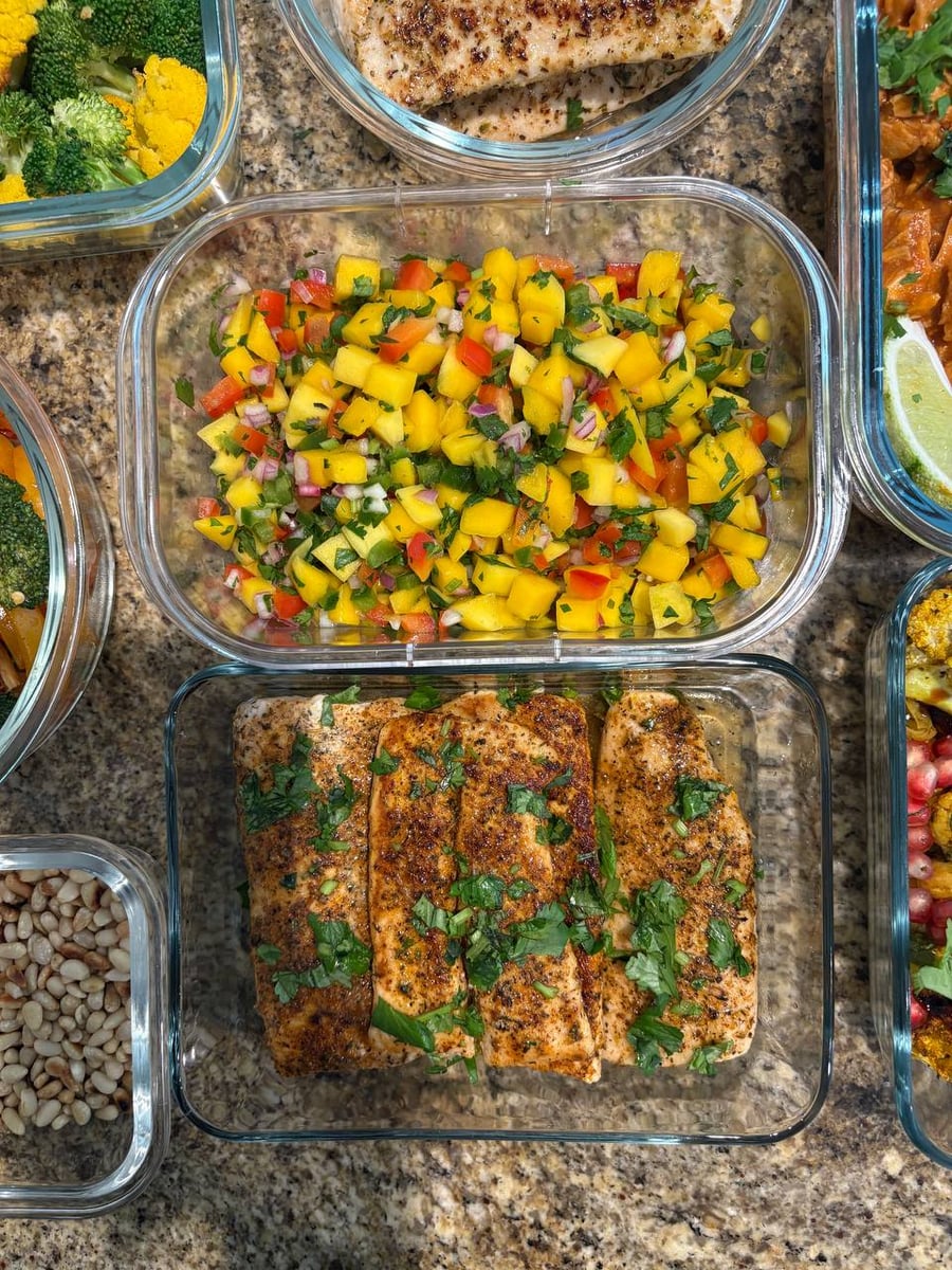 Glass meal prep containers filled with flaky blackened mahi mahi fillets and a vibrant, colorful mango salsa with diced red peppers and fresh herbs.