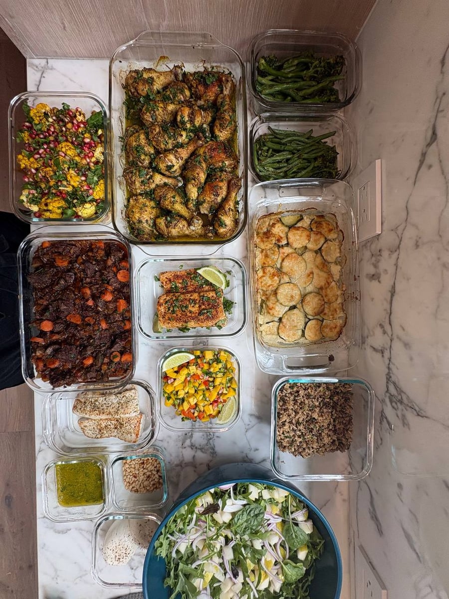 Top-down view of a sophisticated weekly meal prep service selection featuring zaatar chicken, potato gratin, and seasonal sides in clear glass containers.