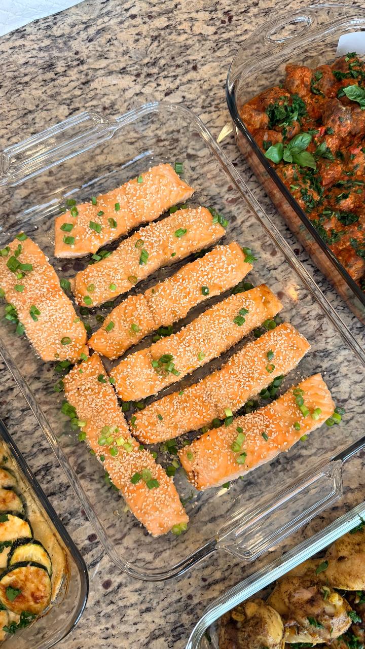 Top-down view of clear glass containers featuring miso-glazed salmon fillets topped with sesame seeds and savory Tuscan-style beef meatballs in rich tomato basil sauce.