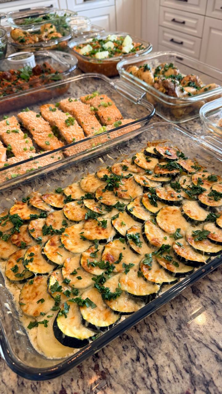 A glass baking dish filled with a layered potato, zucchini, and Gruyere gratin sits beside a container of sesame-crusted miso glazed salmon fillets.