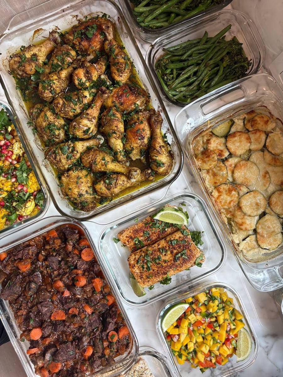 Glass containers featuring zaatar chicken legs, blackened mahi mahi, mango salsa, and a golden potato zucchini gratin, all arranged for a balanced meal prep display.