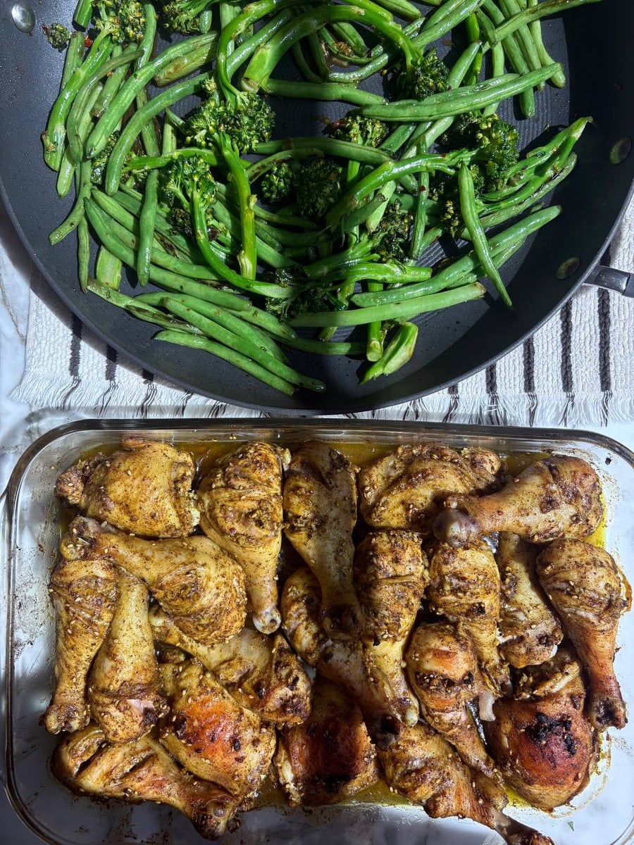 A glass baking dish filled with zaatar spiced roasted chicken drumsticks and a large skillet containing sautéed vibrant green broccolini and French green beans.