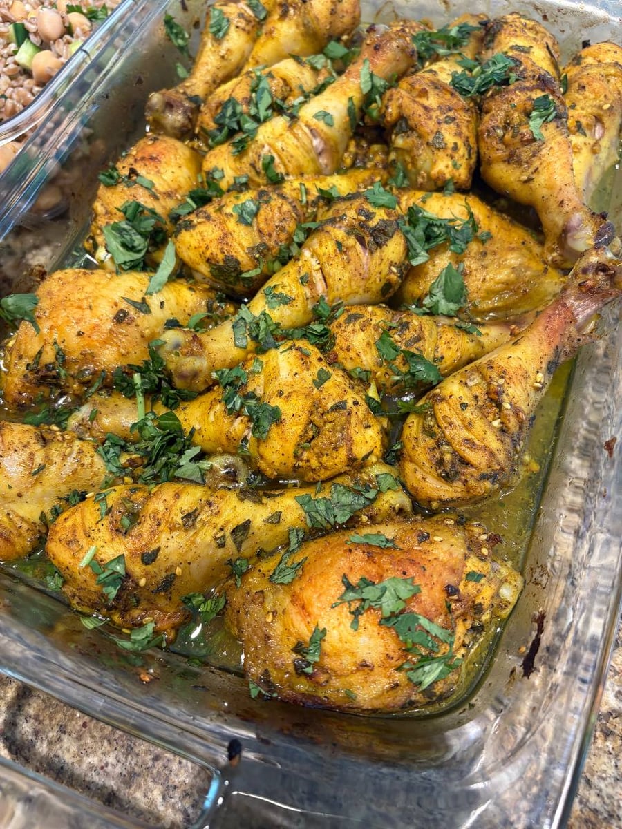 A glass baking dish filled with golden-brown zaatar spiced chicken drumsticks and thighs, generously garnished with fresh chopped green herbs and roasted to perfection.