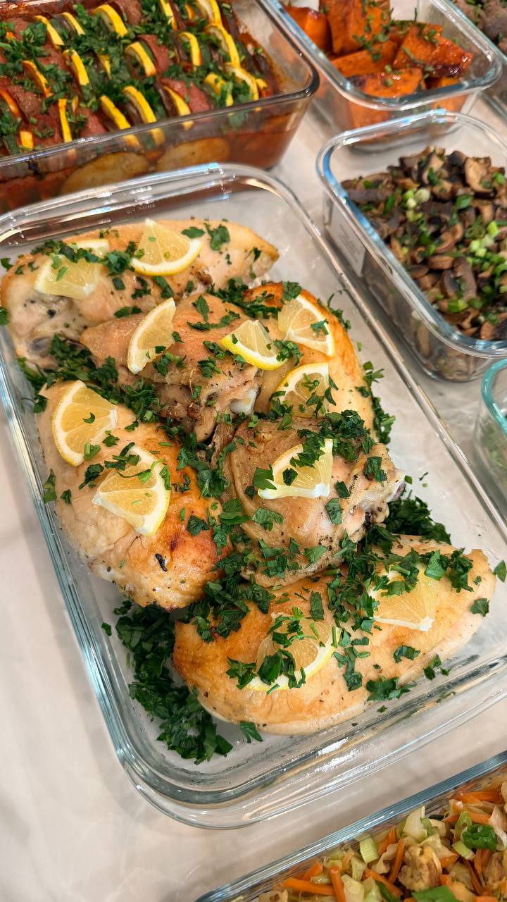A glass tray filled with oven-baked chicken thighs and breasts, garnished with fresh chopped parsley and thin yellow lemon slices.