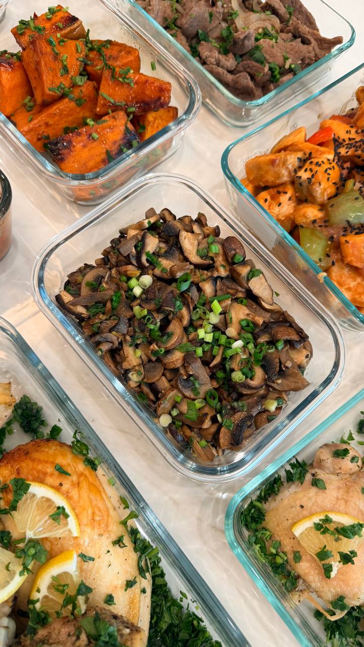 Top-down view of square glass containers holding lemon chicken, beef bulgogi, sweet-sour salmon, oyster mushrooms, and baked sweet potatoes with green garnishes.