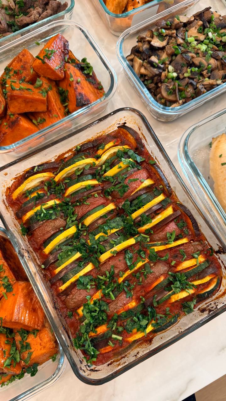 A glass baking dish filled with colorful ratatouille featuring layered eggplant, yellow squash, and zucchini in a savory tomato basil sauce, garnished with fresh herbs.