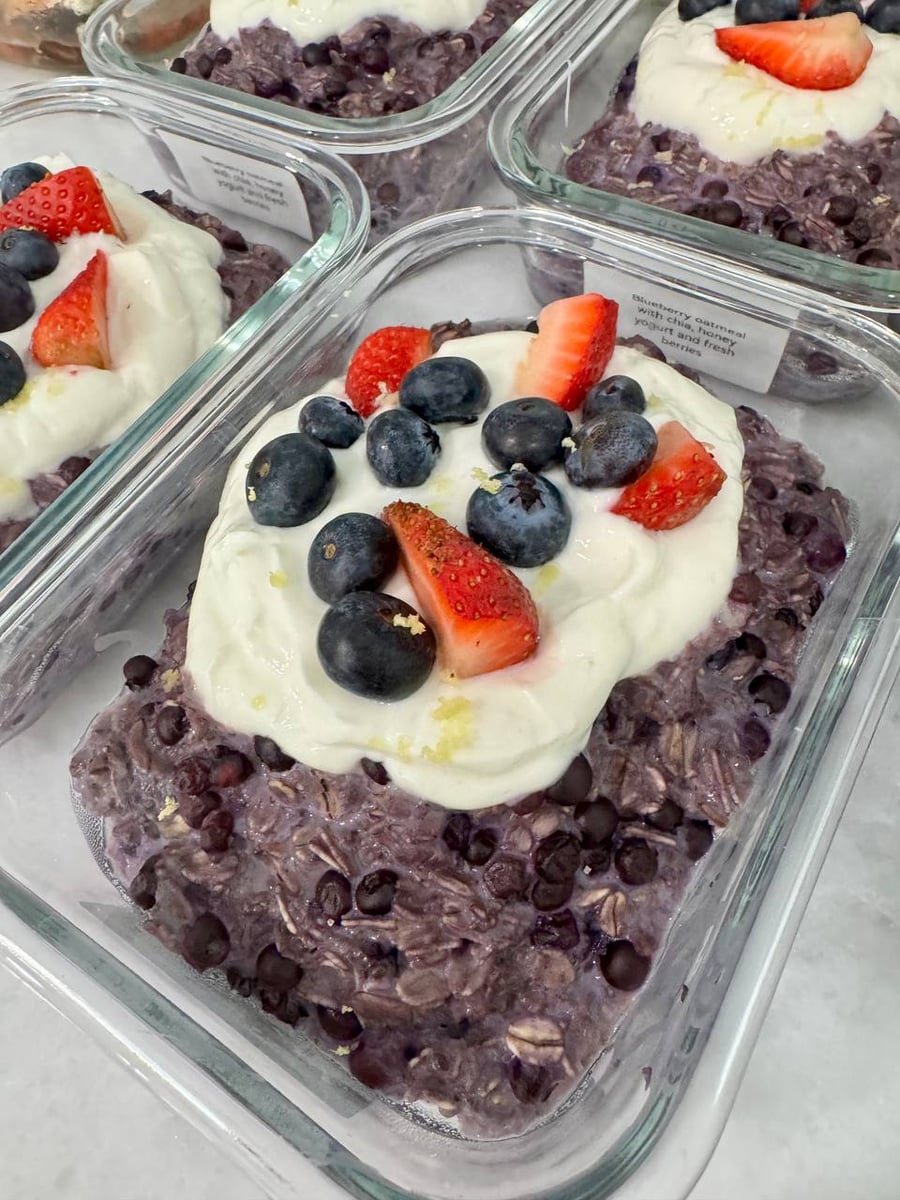 Glass containers of blueberry oatmeal topped with honey yogurt, fresh blueberries, and sliced strawberries, presented perfectly for a nutritious, grab-and-go morning meal.