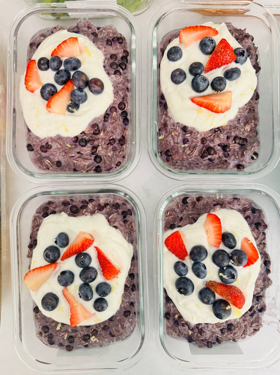Four glass rectangular containers holding blueberry oatmeal topped with thick honey yogurt, fresh sliced strawberries, and plump blueberries arranged neatly for breakfast.