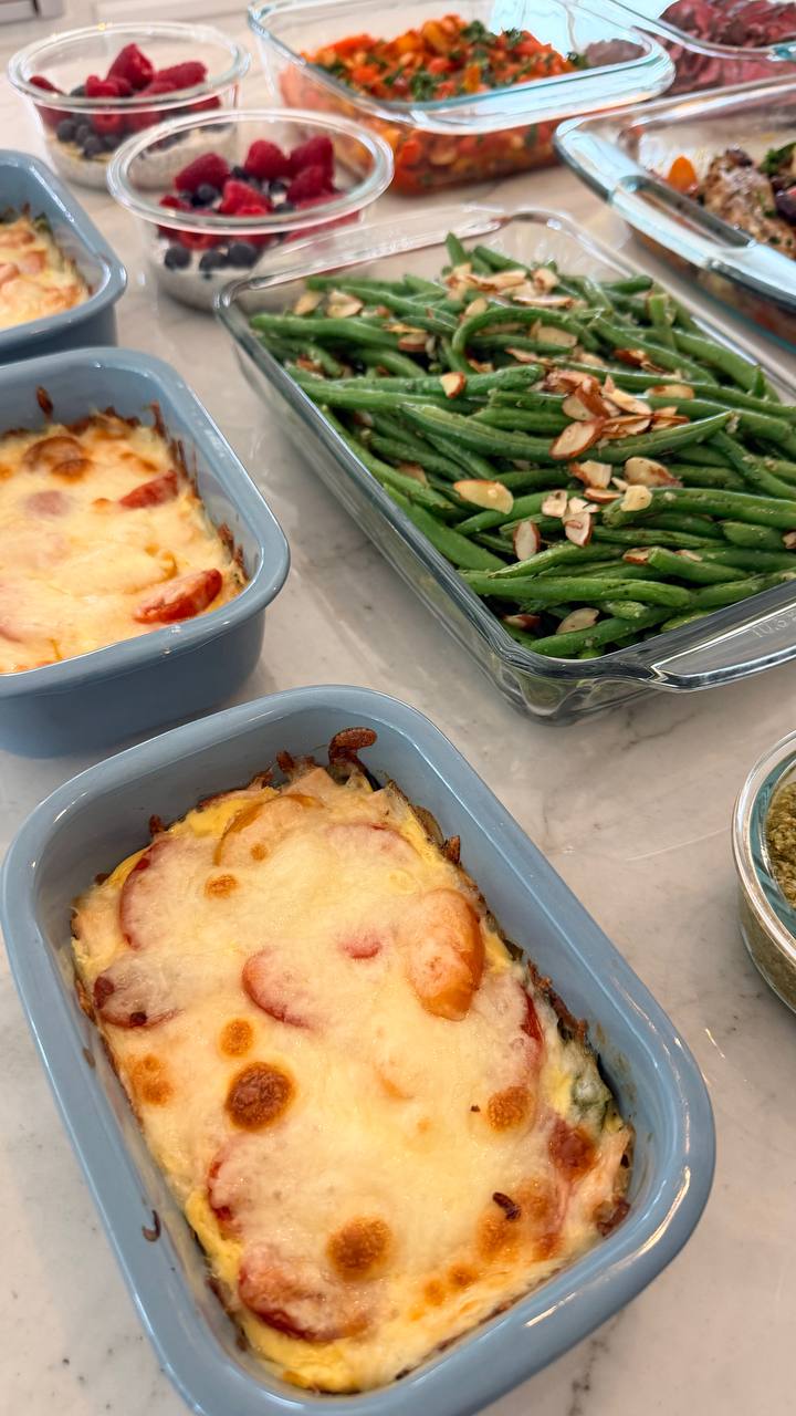 A collection of glass meal prep dishes featuring savory egg frittatas, vibrant green beans almondine, and small bowls of chia overnight oats with fresh berries.