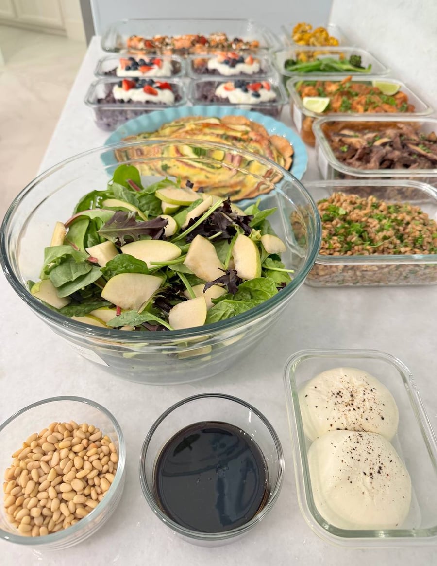 An assortment of prepared dishes including baked salmon, blueberry oatmeal, zucchini quiche, and saucy chicken presented in various glass containers and ceramic dishes.