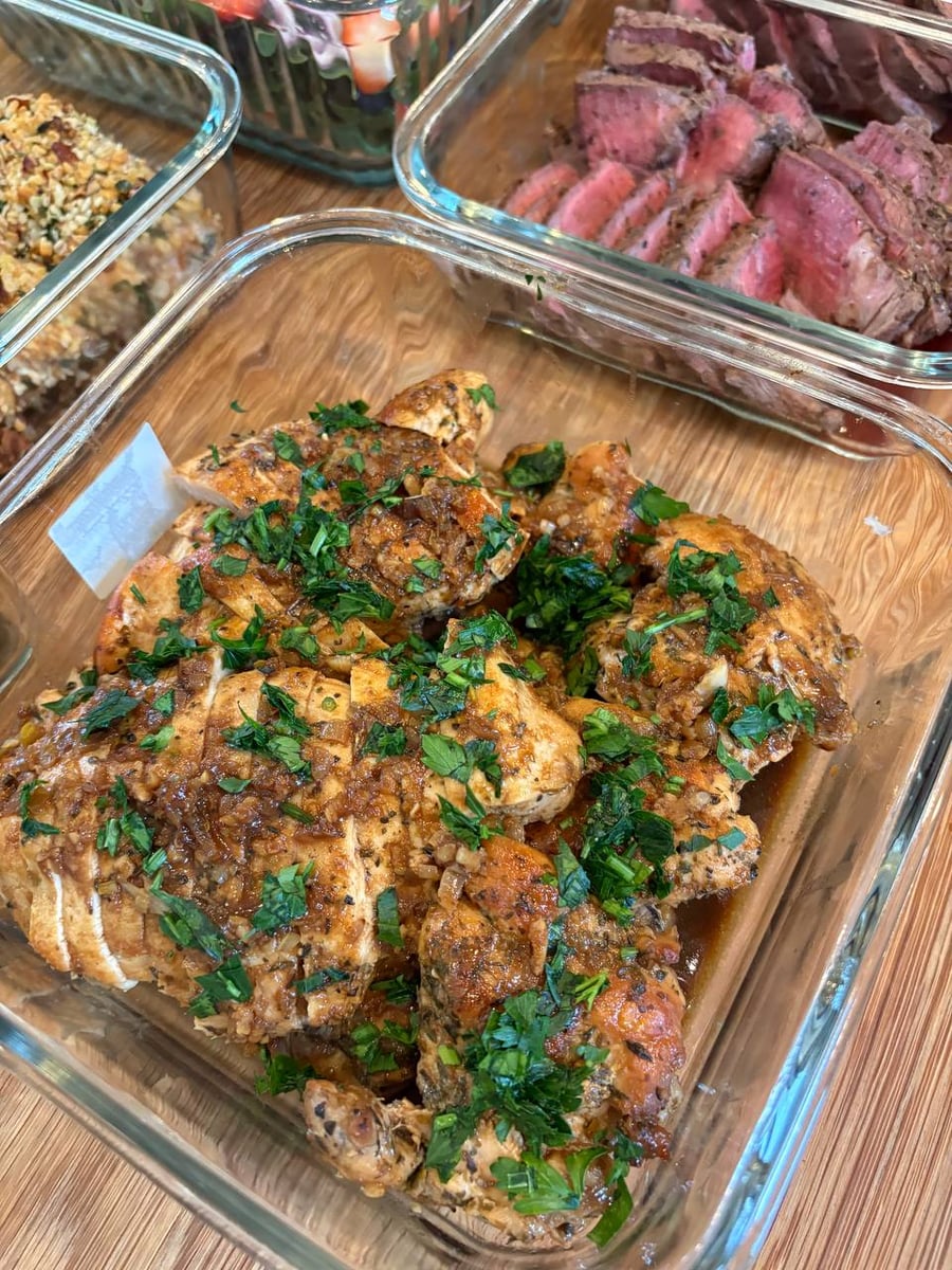 A glass tray of beef burgundy stew, braised balsamic chicken slices, mediterranean cauliflower, and a crisp caesar salad in glass storage containers.