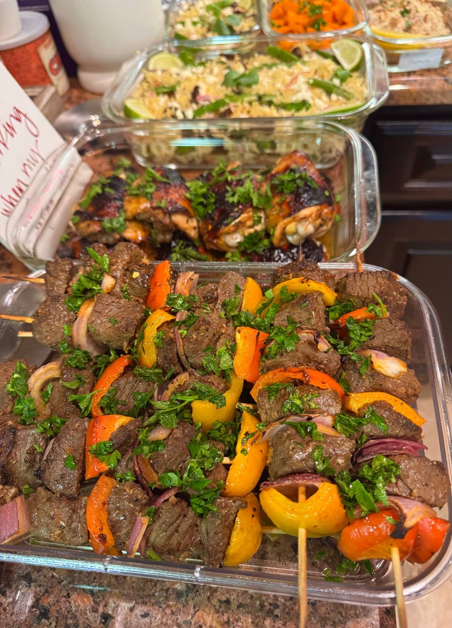 A glass container filled with grilled beef sirloin skewers featuring colorful bell peppers, red onions, and fresh vibrant parsley on top.
