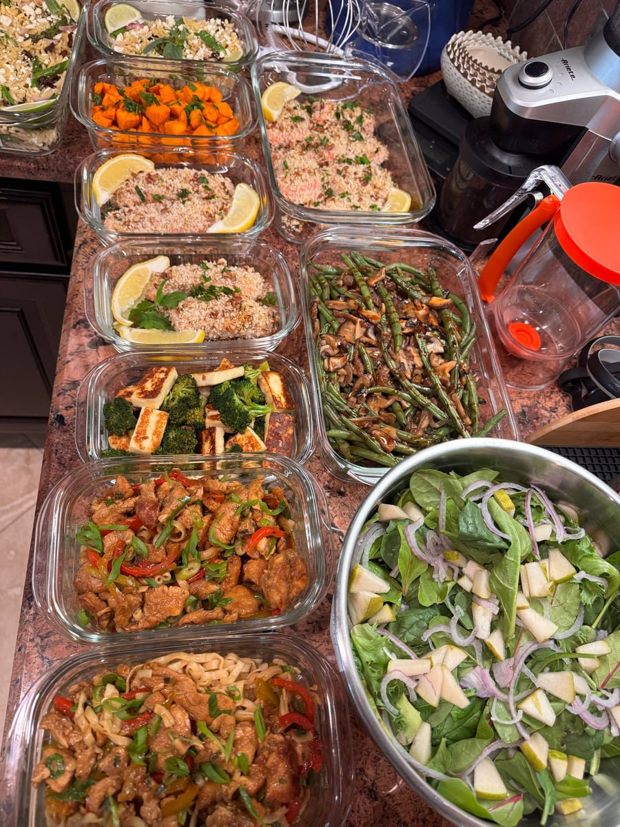 Glass containers filled with pecan-crusted salmon, balsamic chicken, sautéed broccoli with paneer, green beans, sweet potatoes, orzo, noodles, and a fresh pear salad.