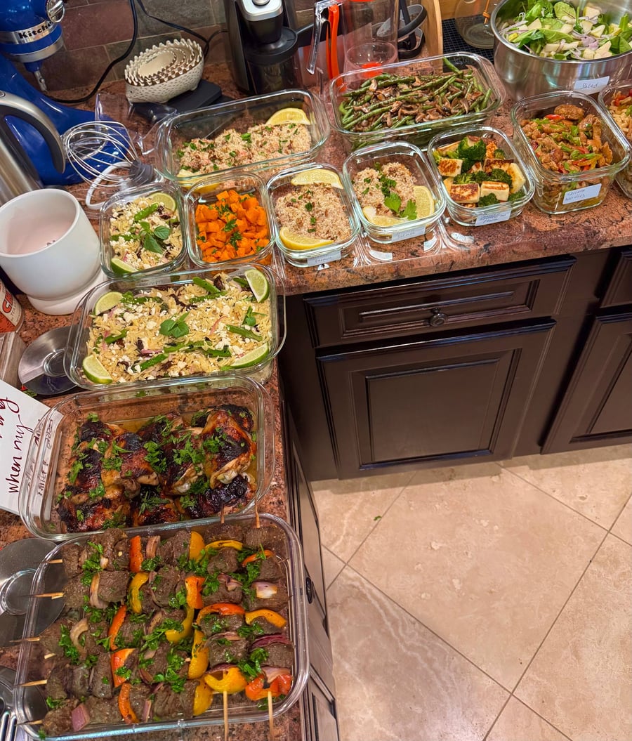 A variety of glass containers holding balsamic chicken, beef skewers, pecan salmon, orzo, green beans, and roasted vegetables prepared for healthy eating.