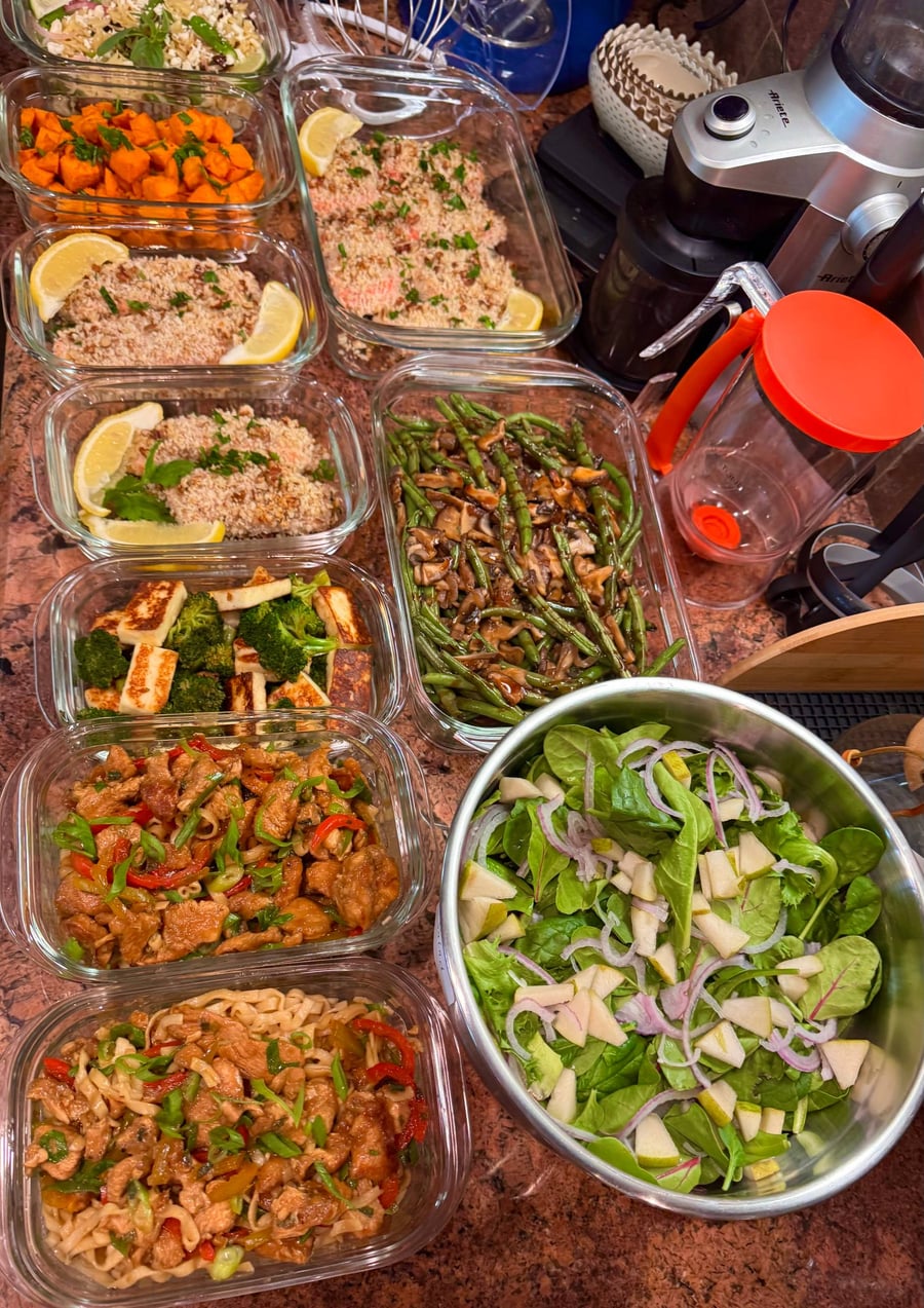 Glass meal prep containers filled with crispy pecan crusted salmon, chicken chow mein, sauteed broccoli with paneer, and balsamic green beans with mushrooms.