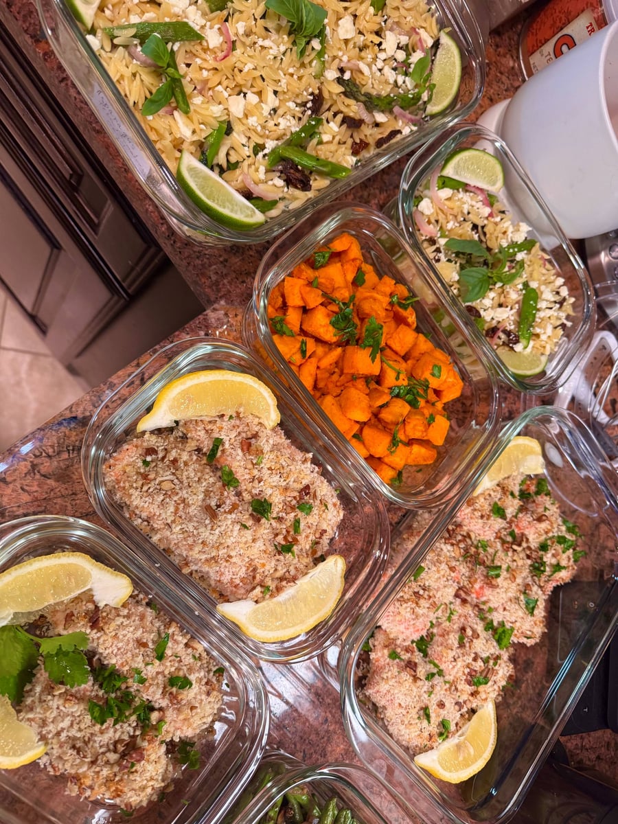 Glass meal prep containers filled with crispy pecan-crusted salmon, orzo pasta with sun-dried tomatoes and feta, and vibrant paprika-spiced sweet potato bites.