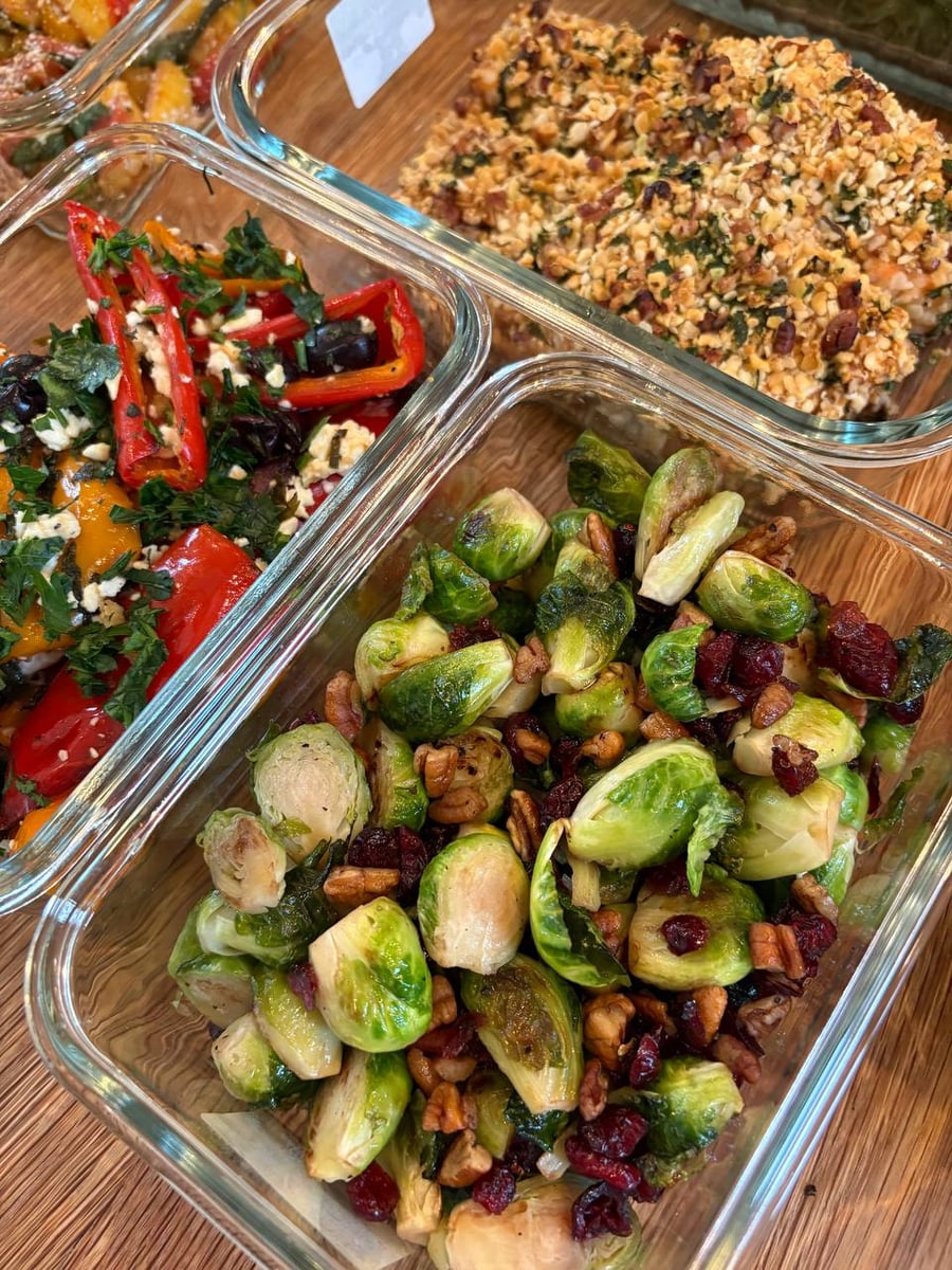 Glass meal prep containers filled with crispy pecan crusted salmon, Mediterranean bell peppers with feta, and maple cranberry pecan roasted Brussels sprouts.