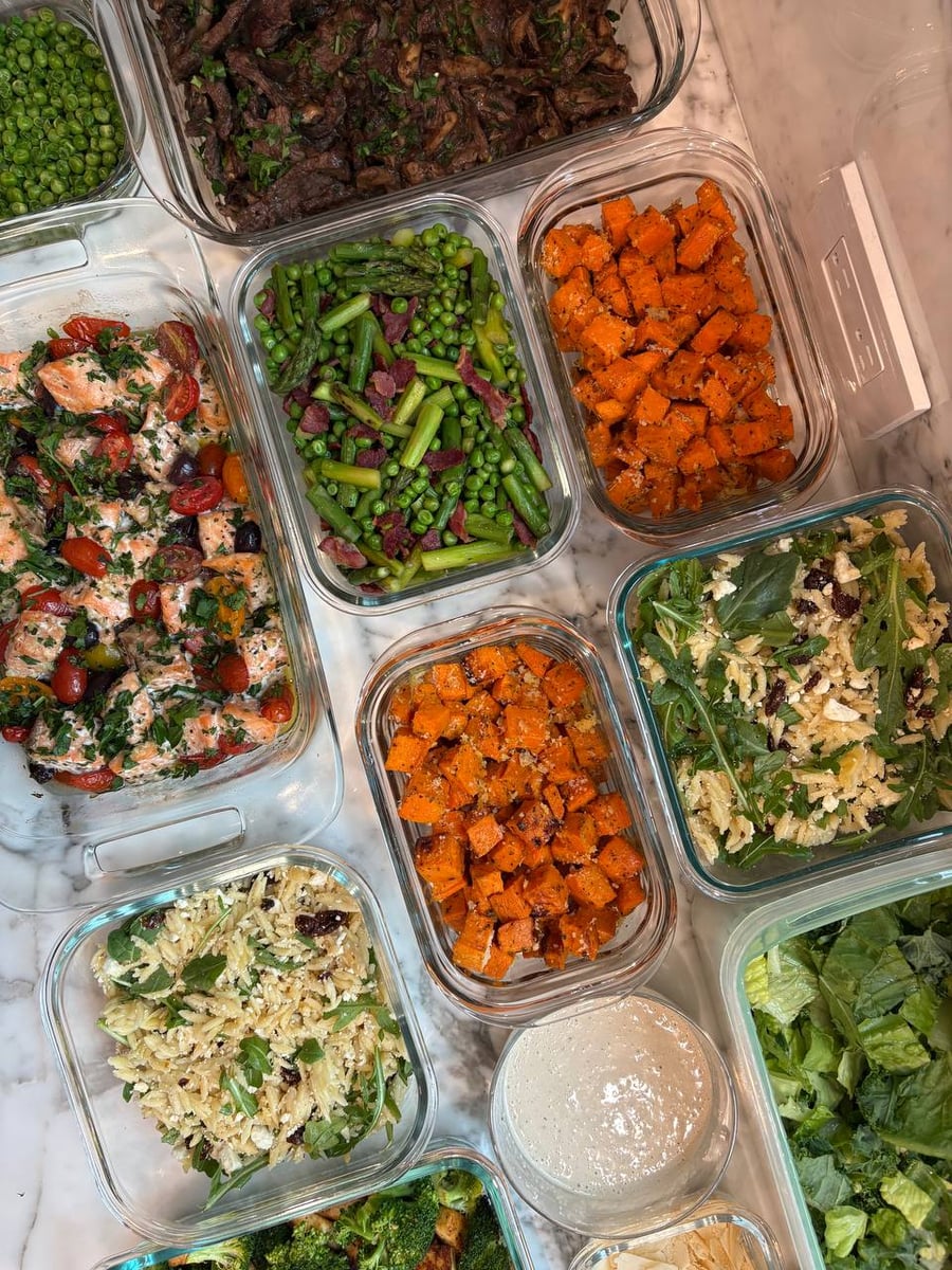 Glass meal prep containers filled with Mediterranean salmon, beef sirloin with mushrooms, seared asparagus with pancetta, sweet potato bites, and orzo arugula salad.