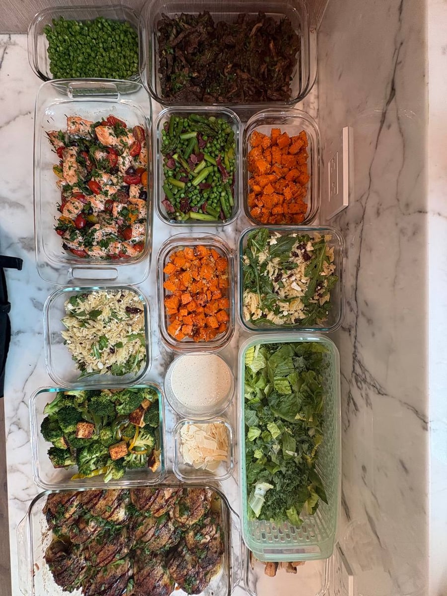 An overhead view of clear glass containers filled with braised balsamic chicken, Mediterranean salmon, beef sirloin, and assorted vegetable and grain sides.