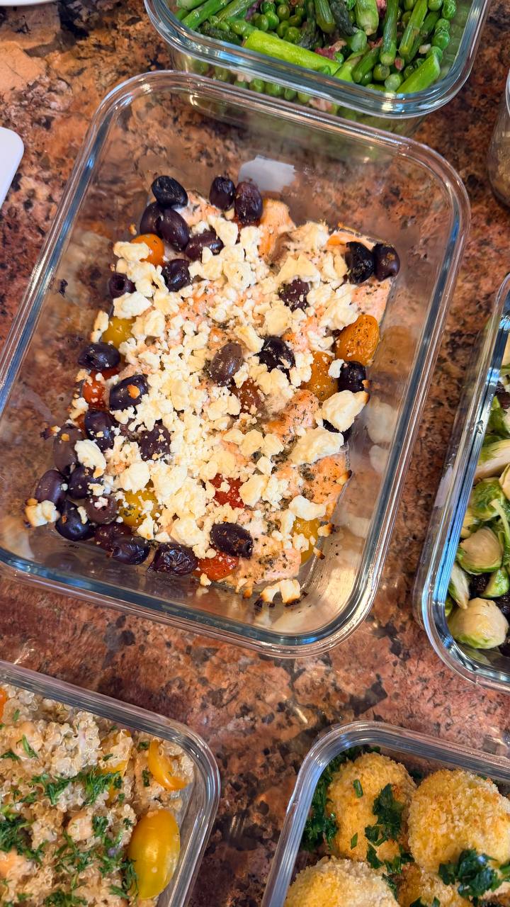 Glass meal prep containers filled with Mediterranean baked salmon bites topped with crumbled feta, black olives, and herbs, arranged on a marble surface.