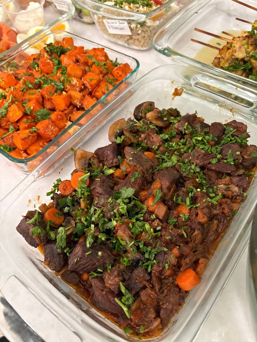 Glass containers holding rich French beef burgundy stew with mushrooms alongside parmesan sweet potato bites topped with fresh green herbs.