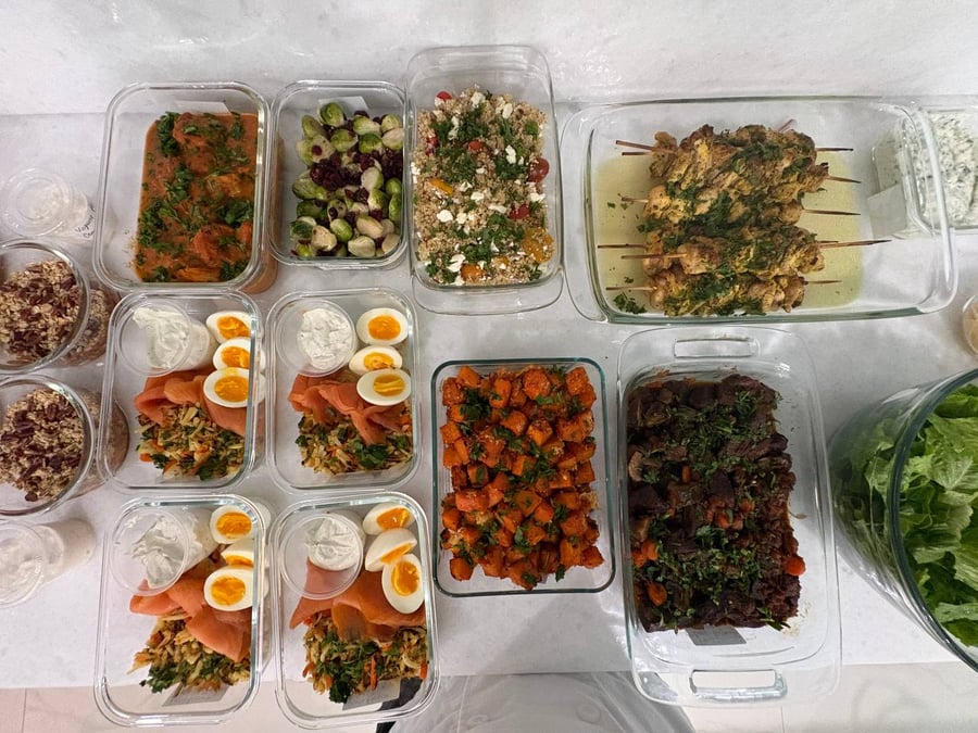 A variety of glass containers holding beef burgundy, chicken souvlaki, salmon breakfast bowls, quinoa salad, maple brussels sprouts, and parmesan sweet potato bites.