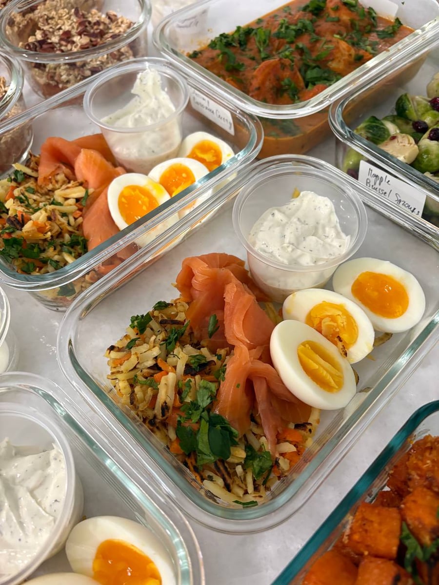 Glass meal containers hold shredded hash browns, thinly sliced smoked salmon, soft-boiled eggs, and a small side cup of creamy yogurt-based dressing.