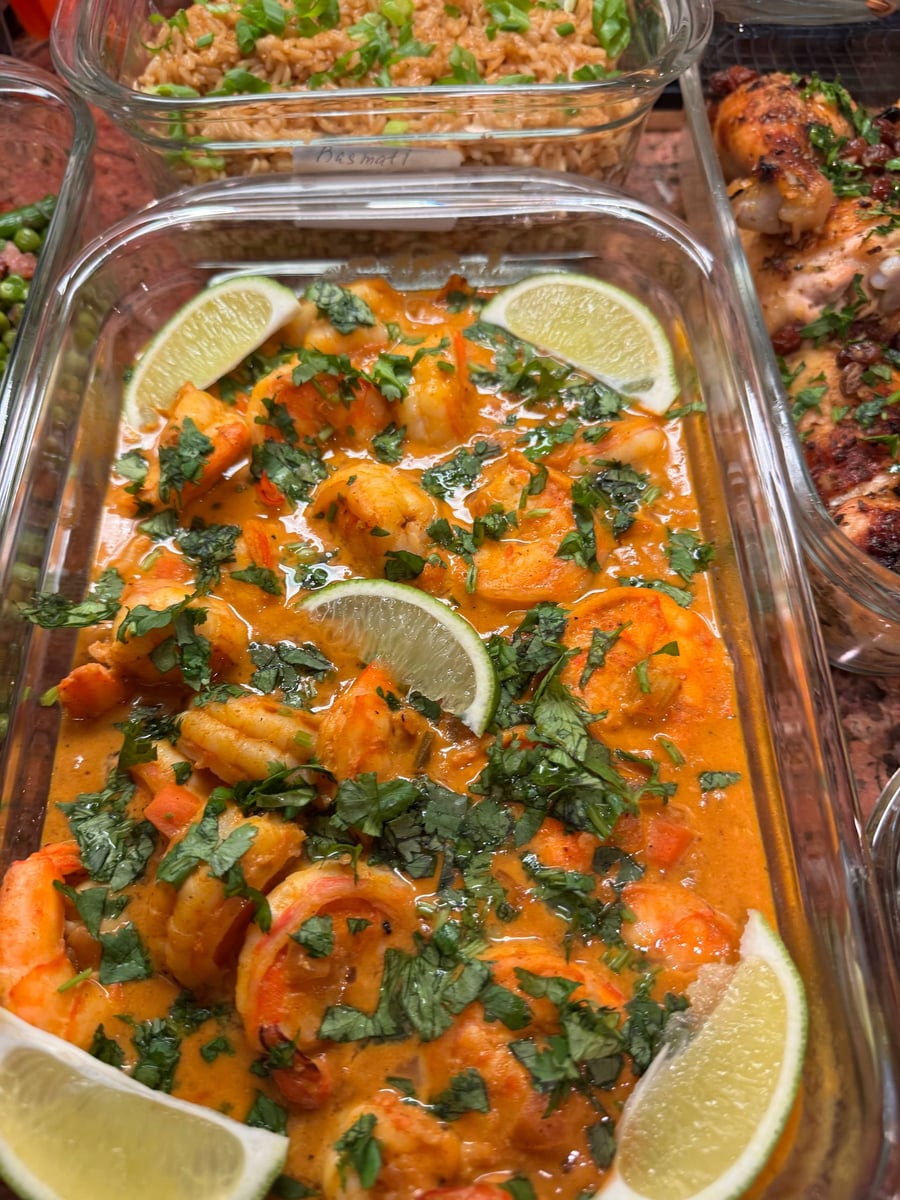 Glass meal prep container filled with creamy curry coconut shrimp garnished with fresh cilantro and vibrant lime wedges, served alongside other prepared dishes.