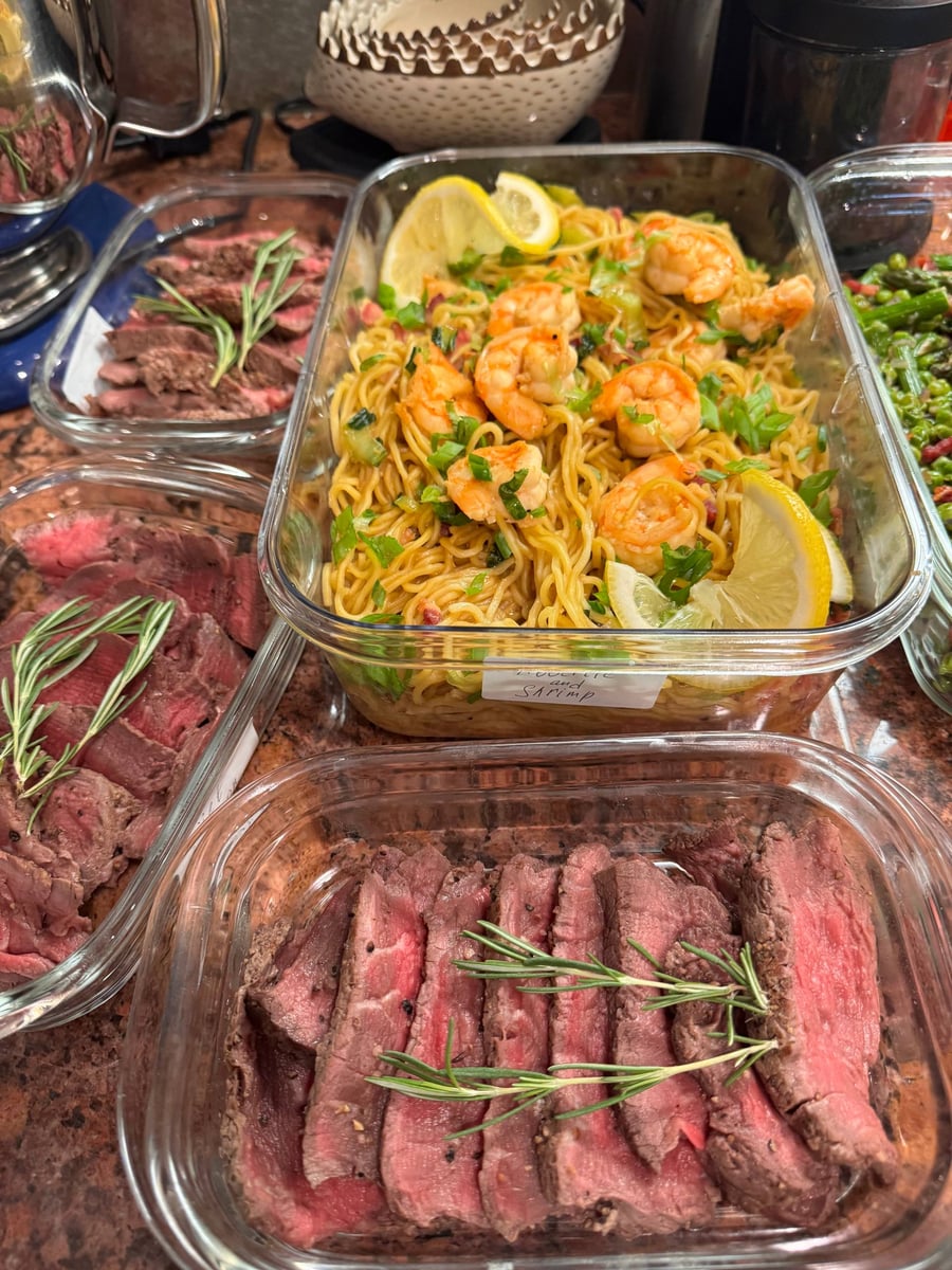 Glass meal prep containers filled with sliced medium-rare filet mignon topped with rosemary and a large container of shrimp and bok choy noodles.