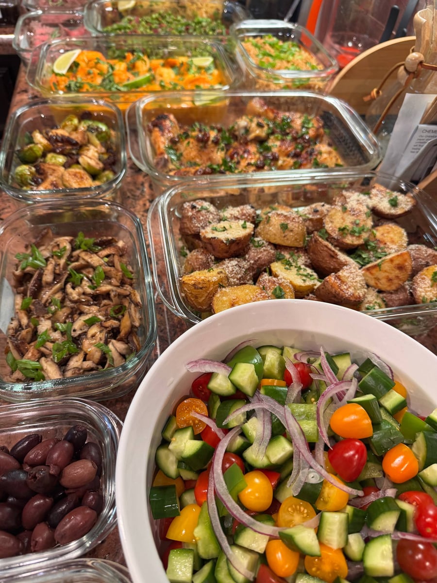 A variety of gourmet meal prep containers featuring orange cranberry chicken, truffle parmesan baby potatoes, garlic shiitake mushrooms, and a fresh Greek salad.
