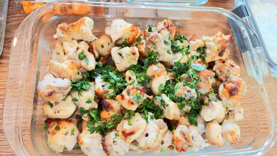 A glass meal prep container filled with golden Greek style chicken skewers, garnished with fresh vibrant green herbs for a healthy meal.
