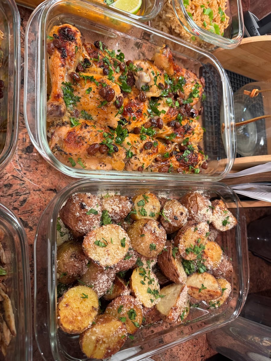 Glass containers hold orange cranberry baked chicken with fresh herbs and truffle parmesan baby potatoes, presented in organized, transparent meal prep dishes.