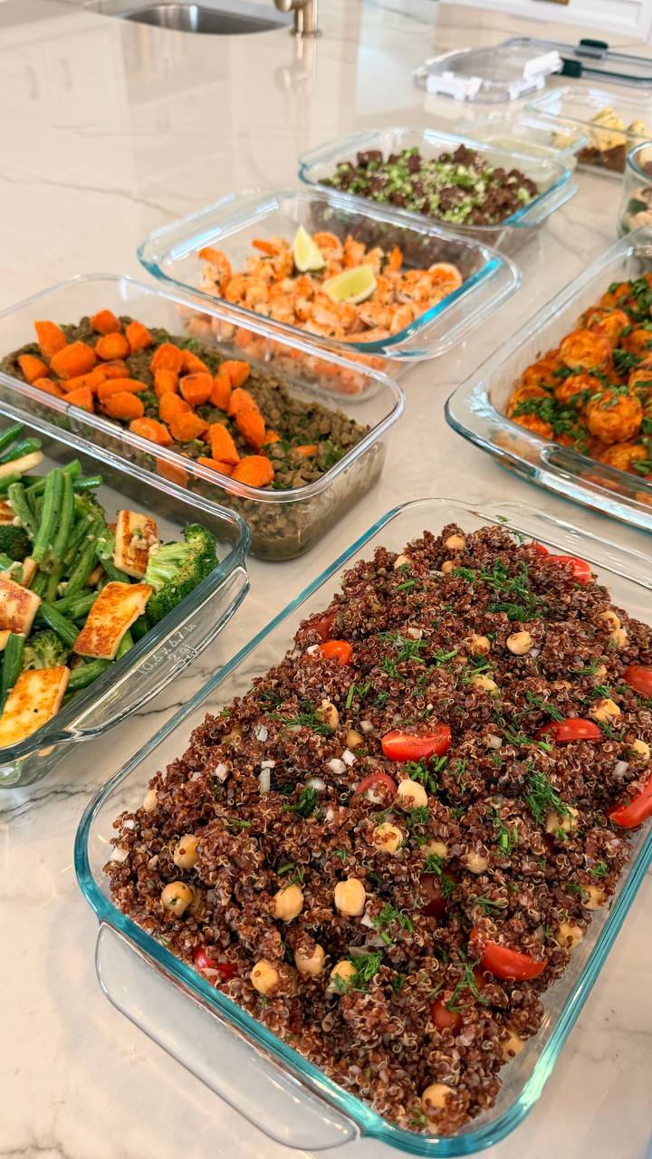 Glass containers display various dishes including quinoa with tomatoes, shrimp with lime, tender meatballs in sauce, sautéed paneer with vegetables, and rustic lentil stew.