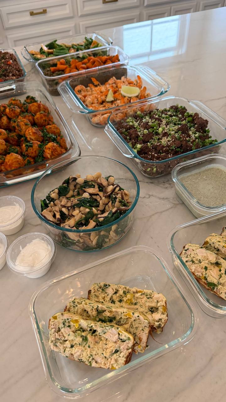 An assortment of glass containers filled with turkey meatballs, lime shrimp, ginger beef, sauteed spinach, egg bake, and various healthy prepared side dishes.