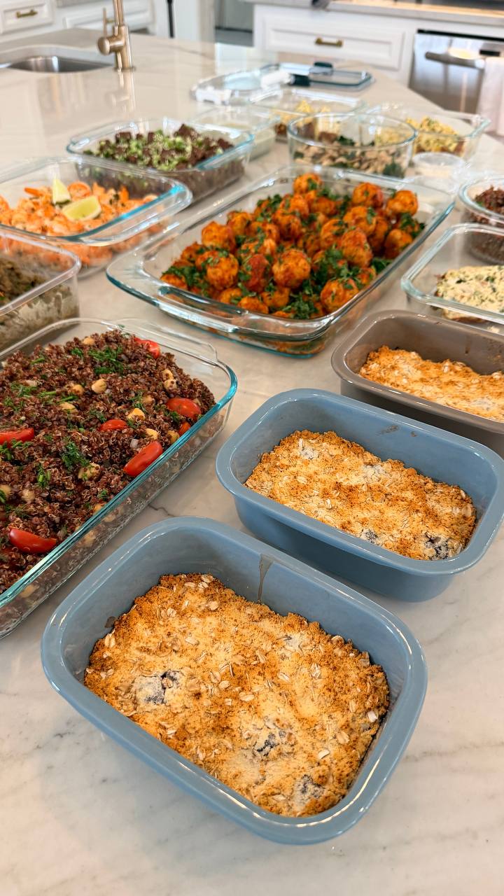 A collection of glass meal prep containers featuring Tuscan turkey meatballs, quinoa with tomatoes, ginger beef, and berry oat crumble bakes.