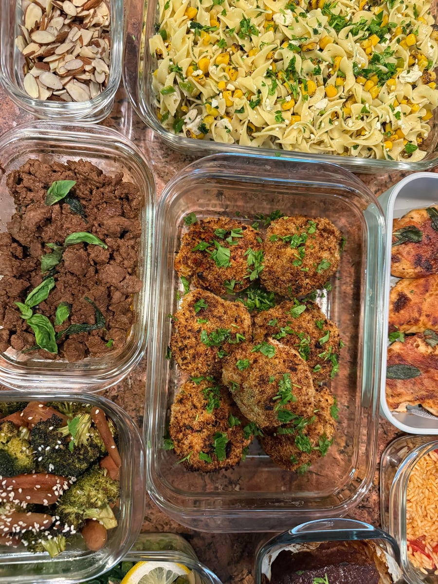 Feta crumbles and charred corn through wide egg noodles, breaded shrimp cakes filling the tray below.
