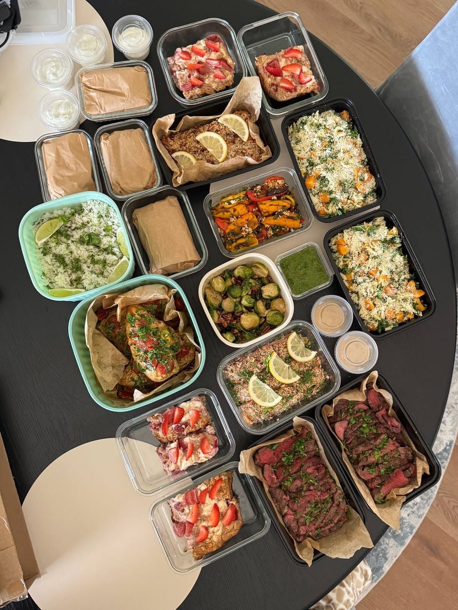 Round table carries the whole delivery: pesto chicken, filet mignon, orzo trays and strawberry oats.