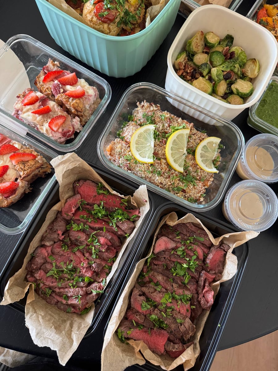 Parsley scatters over filet mignon sliced medium-rare on parchment, strawberry baked oats to the left.