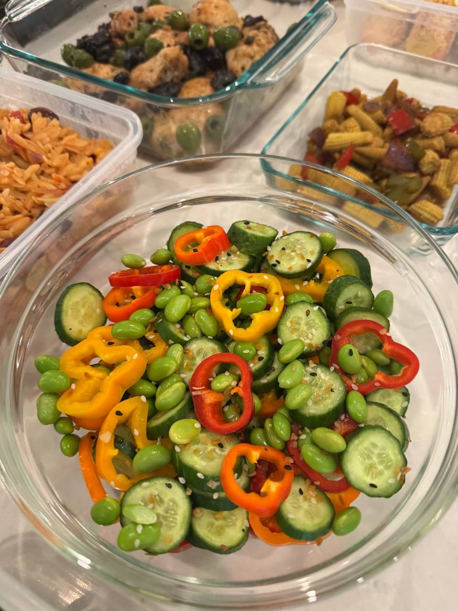 Sesame seeds dust cucumber coins, edamame and rings of baby bell pepper in a wide glass bowl.