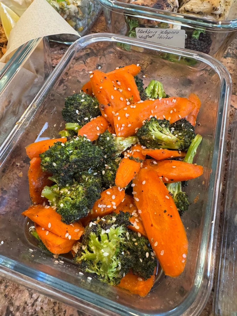 Sesame dots roasted broccoli florets and thick carrot slices, with browned edges and glossy seasoning.