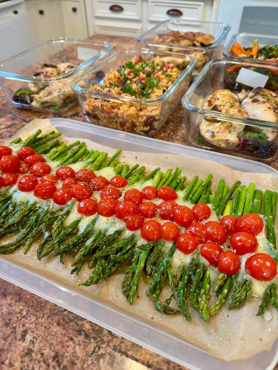 Cherry tomatoes stripe mozzarella-covered asparagus spears, their green tips arranged in even rows across parchment.