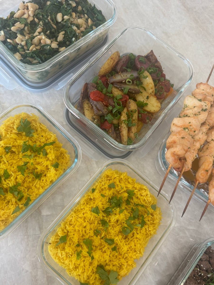 Two pans of turmeric rice sit below roasted fingerling potatoes and tomatoes, spinach with butter beans and chicken skewers.